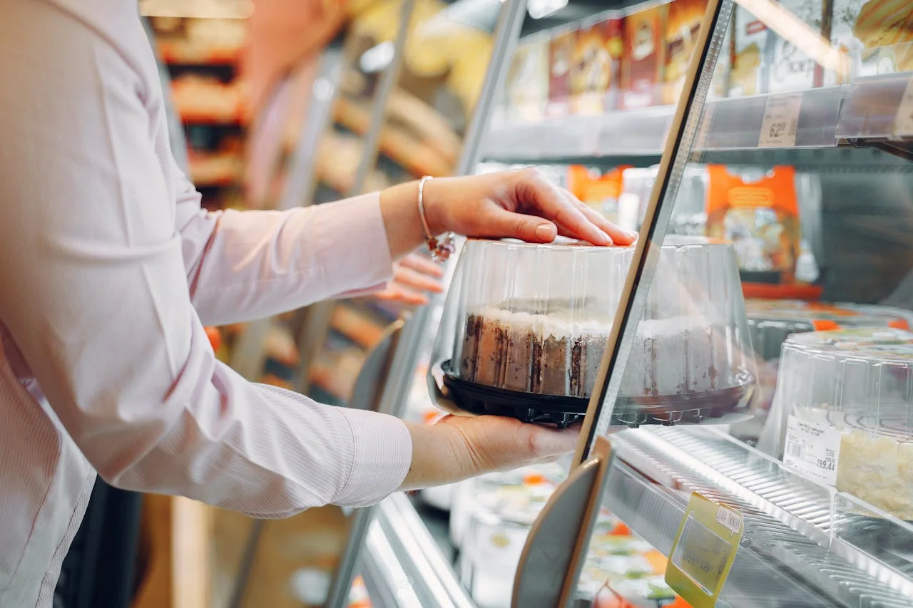 Shopper selecting a packaged cake from a convenience-store display case