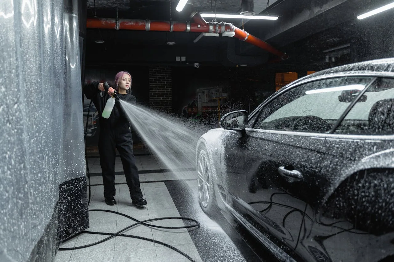 Employee pressure-washing a car inside a wash bay