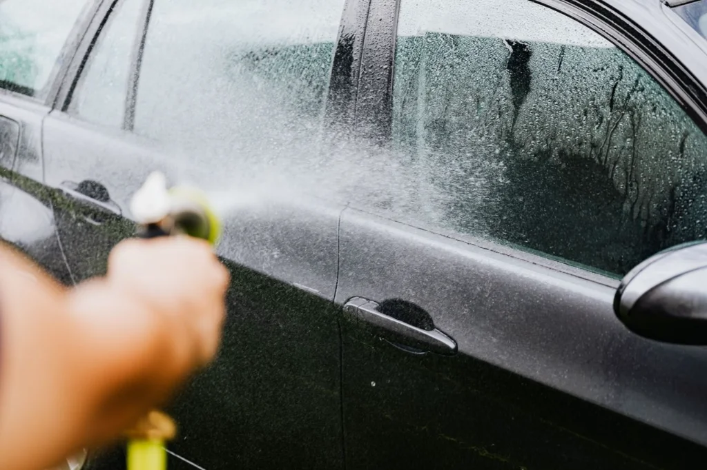 Worker pressure-washing the side of a car